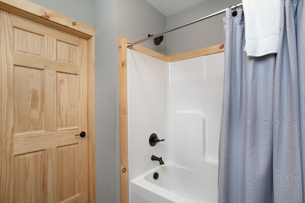 A bathroom with a wooden door, a white bathtub, and a shower curtain.