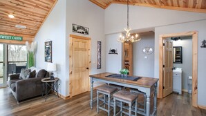 L’intérieur d’une cabane est doté d’un plafond en bois, d’un coin repas agrémenté d’un lustre, d’un canapé et d’une petite table avec une lampe.