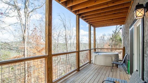 Une terrasse en bois avec un jacuzzi et des chaises, donnant sur une zone boisée.