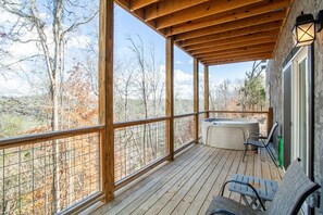 A wooden deck with a hot tub and chairs, overlooking a forested area.