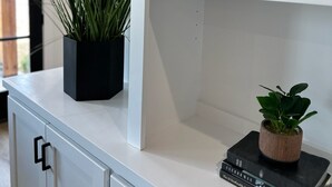 Un mueble blanco con una planta en una maceta negra y una maceta de madera pequeña con una planta verde sobre un libro titulado 'The 21 Irrefutable Laws of Leadership' de John C. Maxwell.