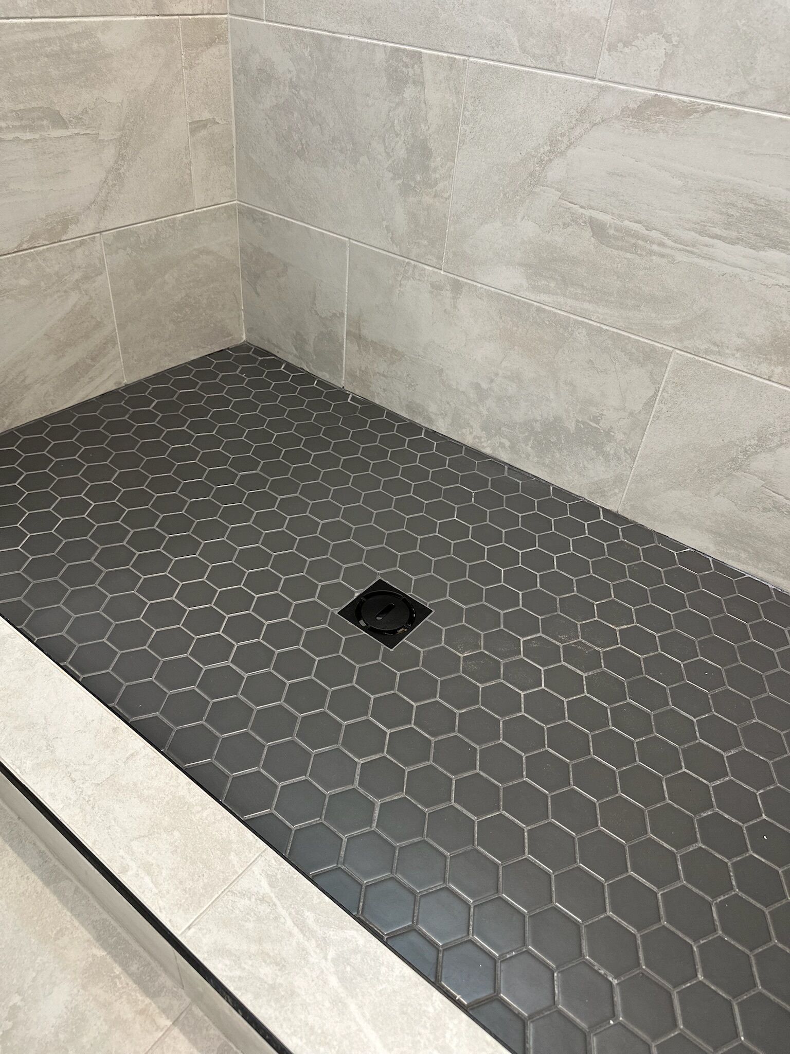 Ducha con azulejos hexagonales y desagüe central.