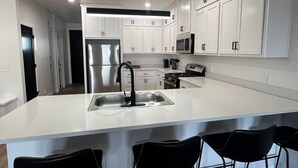 Cocina moderna con armarios blancos, una isla grande con taburetes de bar, electrodomésticos de acero inoxidable e iluminación empotrada en el techo.
