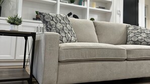 Una sala de estar con un sofá color beige, una mesita con una planta y un estante blanco al fondo.