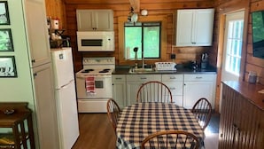 A cabin-style kitchen with white cabinets, a stove, a microwave, and a dining table with chairs.