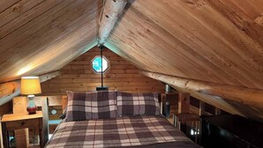 An attic bedroom with a checkered bedspread, a wooden ceiling, and a skylight.