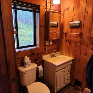 A wooden cabin bathroom with a toilet, sink, and window.