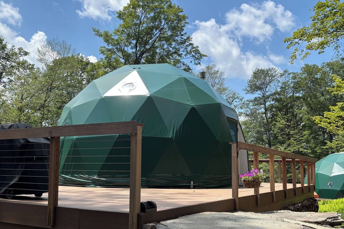 A geodesic dome structure with a wooden deck and a stone pathway leading to it.
