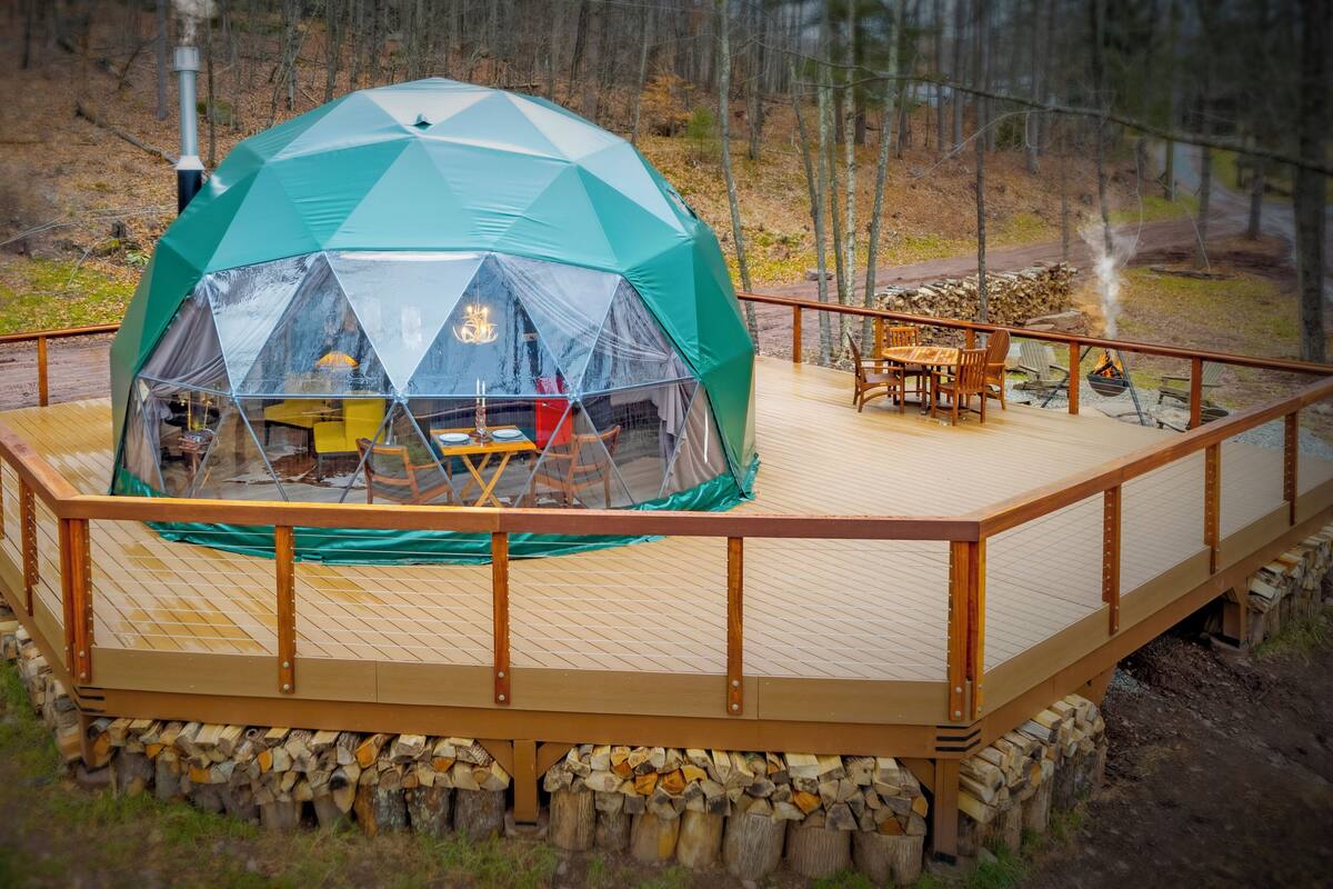 A geodesic dome tent with a wooden deck and outdoor furniture.