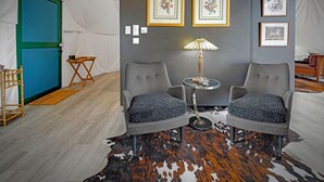 A room with two grey armchairs, a small round table with a lamp, framed pictures on the wall, a blue door, and a cowhide rug. - Domes at Catskills (Swan Lake)