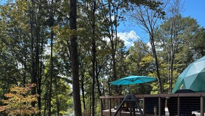 A wooden deck with Adirondack chairs, a swing, and a fire pit. - Domes at Catskills (Swan Lake)