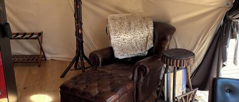 A tent interior with a leather armchair, a lamp, a small table, and a patterned rug.