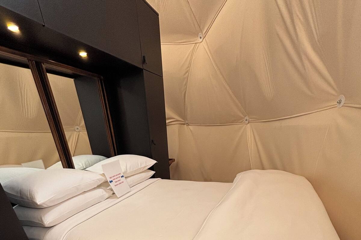 A neatly made bed with white linens and pillows, a dark headboard, and a wooden floor.