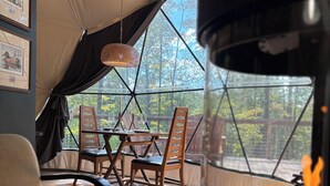 A cozy tented room with a dining table, chairs, and a glass fireplace. - Domes at Catskills (Swan Lake)