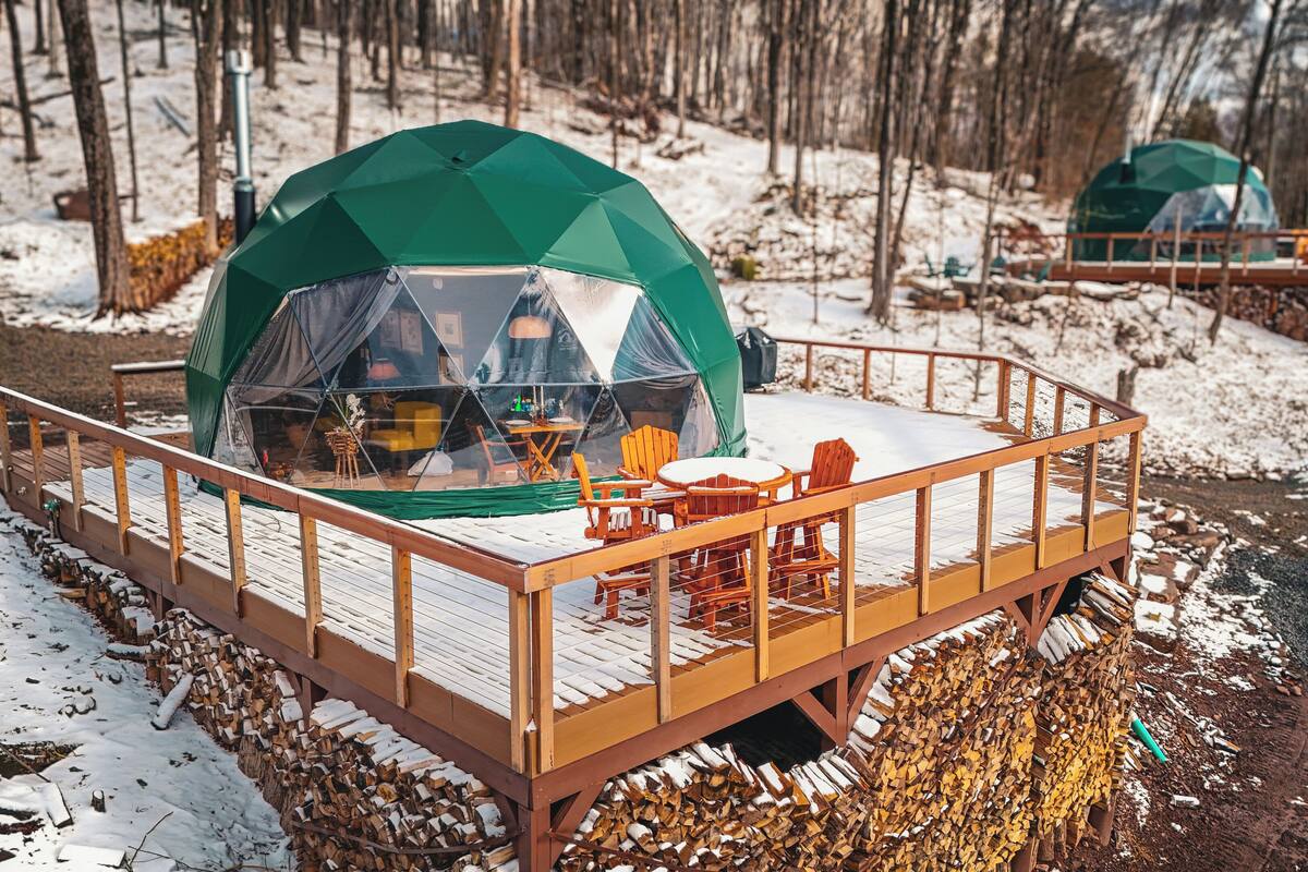 A snow-covered wooden deck with a green dome tent and wooden chairs.