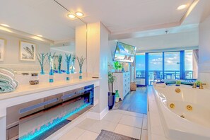 Un baño moderno con una bañera grande, suelo con calefacción y un televisor montado en la pared.