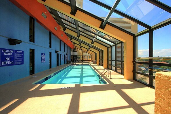 Una piscina interior con techo de cristal, rodeada de paredes azules y vista al cielo.