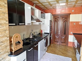 Een praktische keuken met een fornuis, spoelbak en wasmachine, houten kastjes en een decoratieve deur.