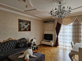 Een woonkamer met een donkere bank, een televisie, een kroonluchter en een pluche panda.