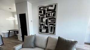 Uma sala de estar moderna com um sofá bege, uma obra de arte geométrica na parede e piso de madeira.