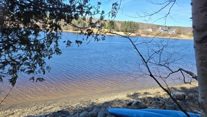A rocky shoreline with a large body of water, a blue kayak, and a house in the background.