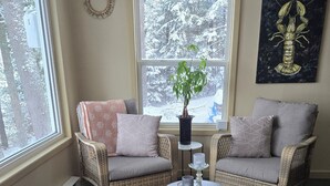 A cozy living room with wicker furniture, a central coffee table, and a view of a snowy landscape through a large window.