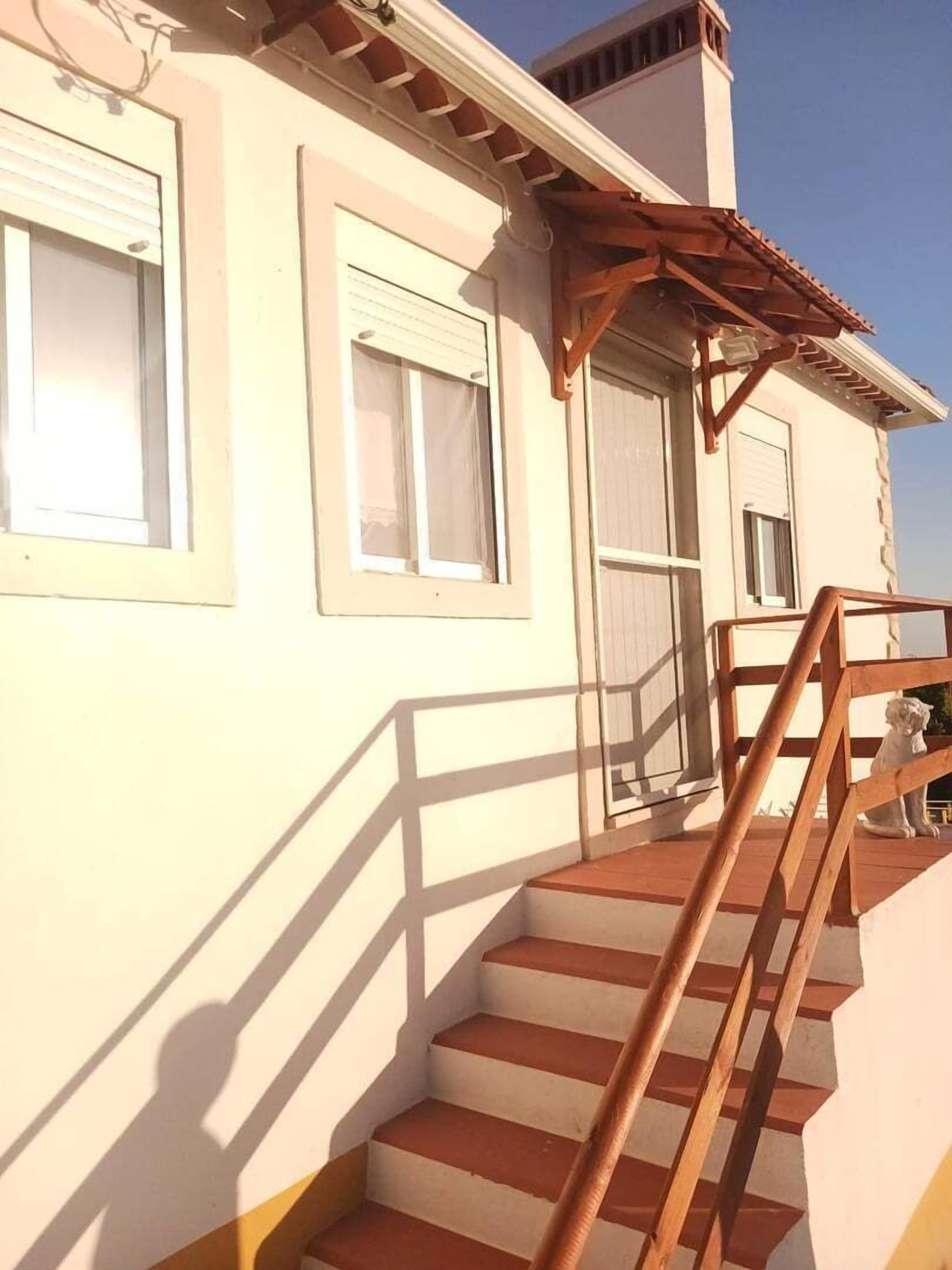A staircase leading to a building with a white facade, wooden railings, and a small statue on the porch.