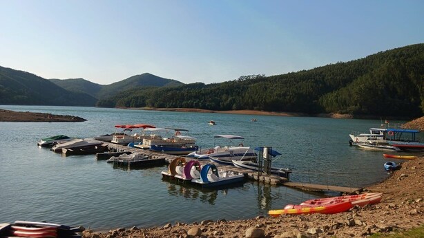 A lakeside dock with various boats and a rocky shore.