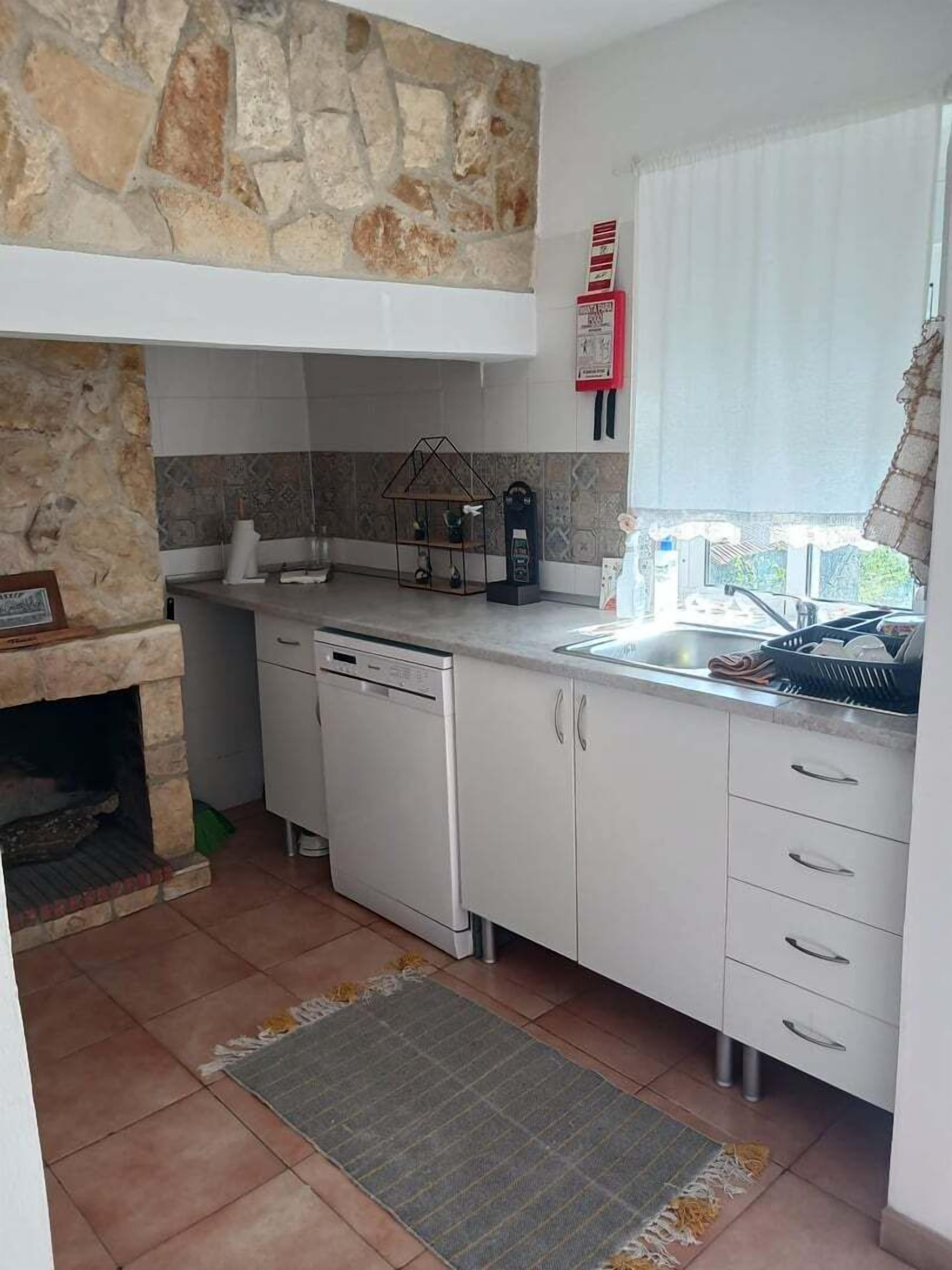 A compact kitchen with a stone accent wall, a built-in dishwasher, and a window with a view of the outside.