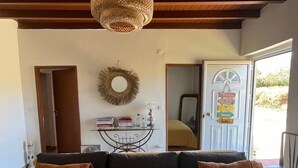 A cozy living room with a sofa, a table with books and decorative items, a hanging light fixture, and a door with a sign.