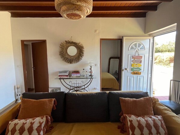 A cozy living room with a sofa, a table with books and decorative items, a hanging light fixture, and a door with a sign.