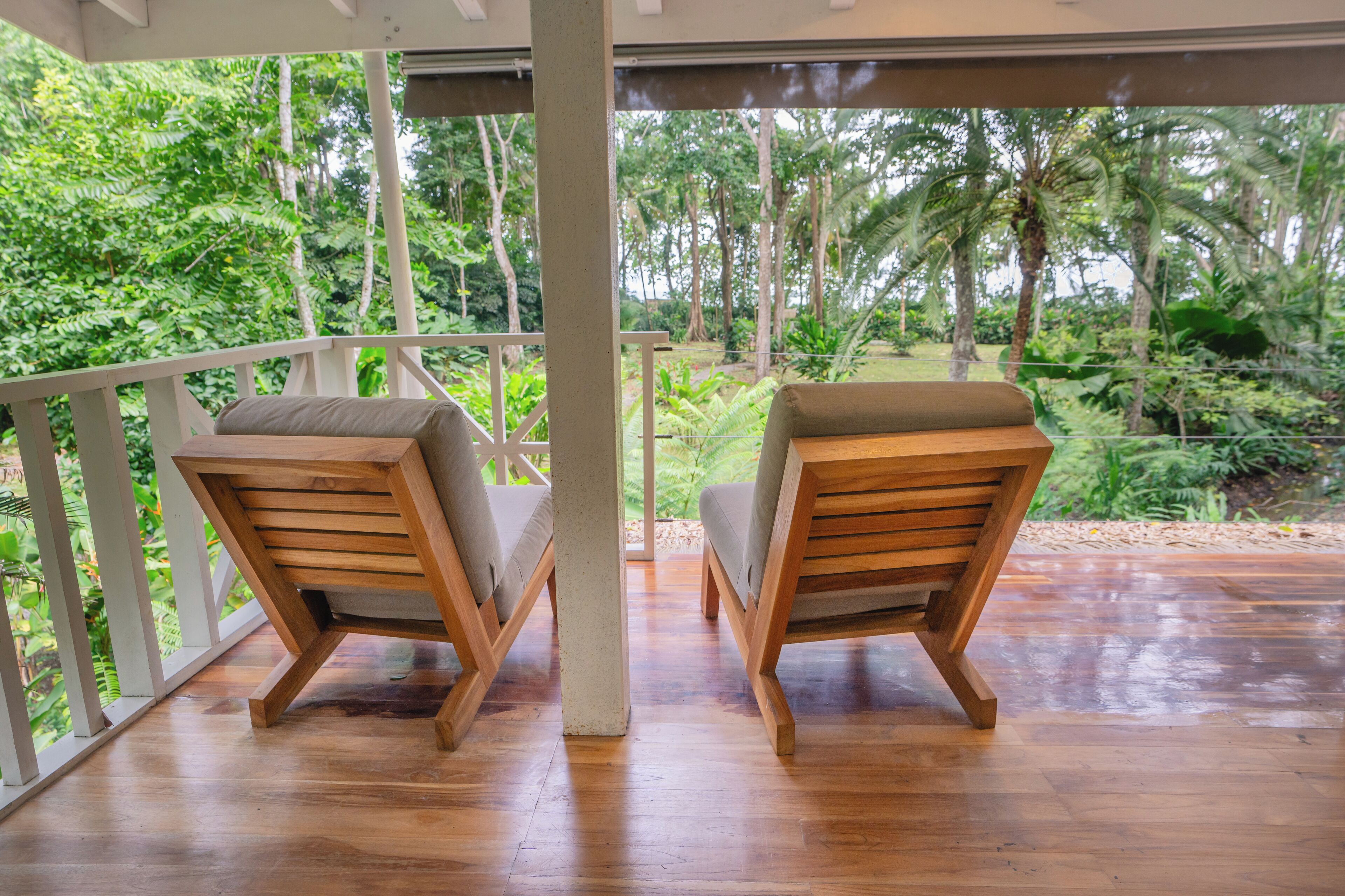 A wooden deck with two cushioned chairs facing a lush garden.