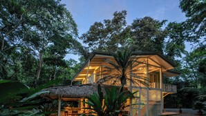A wooden house with a thatched roof, surrounded by dense tropical vegetation. - Villa Oasis (Cahuita)