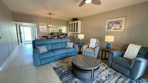 A living room with a blue sofa, two armchairs, a coffee table, and a dining area with a kitchen in the background.