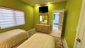 Un dormitorio con dos camas, un aparador, un televisor y una puerta que da a otra habitación.