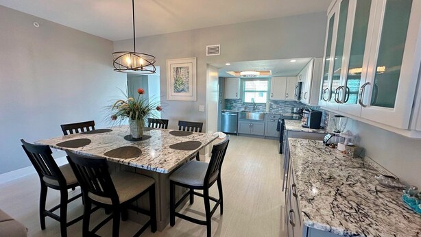 A modern kitchen with a marble countertop, a dining area with a round table and chairs, and a view into the living area.