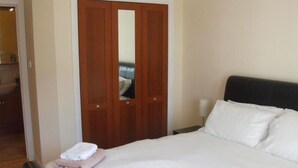 Hotellihuone, jossa on sänky, yöpöytä, peili ja puinen vaatekaappi.