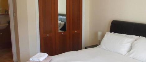 A hotel room with a bed, a nightstand, a mirror, and a wooden wardrobe.