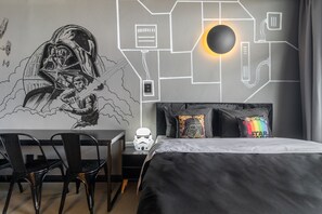 Une chambre avec une fresque murale sur le thème de Star Wars, un lit avec des oreillers noirs et multicolores, et un bureau avec des chaises.