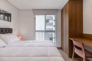 A bedroom with a bed, a desk, a chair, a window with a view of buildings, and a wall-mounted lamp. - Miq277-1107 in S o Paulo (São Paulo)