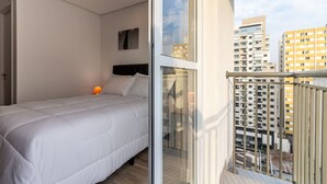 Ein Schlafzimmer mit Bett, Nachttisch, Fenster und Blick auf die Stadt.