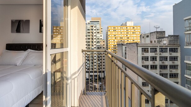 Ein Balkon mit einem Bett, Blick auf hohe Gebäude und einem Metallgeländer.