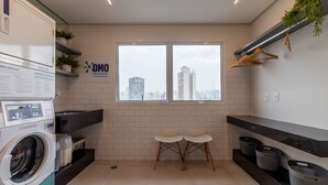 A laundry room with a washing machine, two stools, a window with a city view, and shelves with plants and baskets. - Miq277-1107 in S o Paulo (São Paulo)