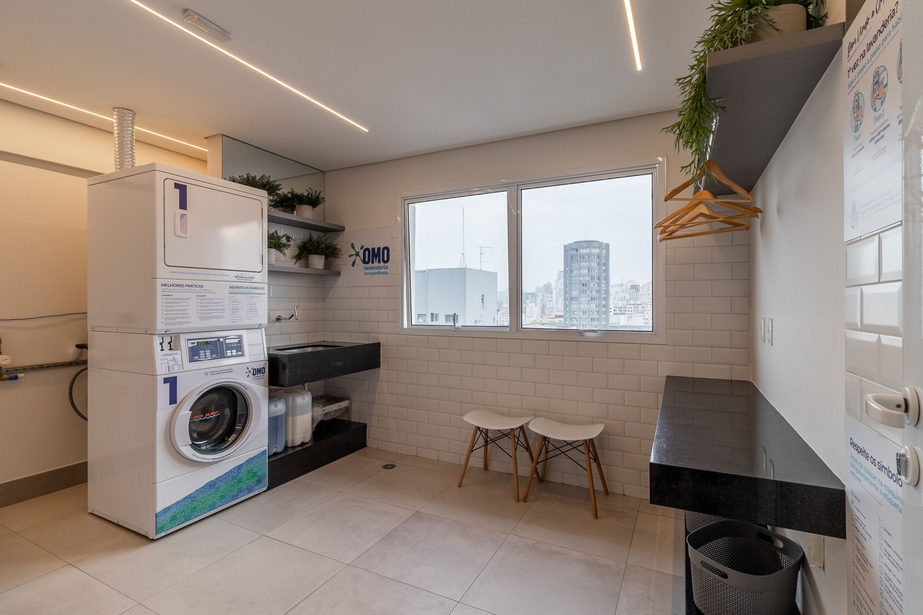 Une buanderie moderne équipée d’un lave-linge à chargement frontal, d’un évier et d’une fenêtre donnant sur la ville.