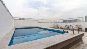 A rooftop swimming pool with a clear blue water, surrounded by a stone deck, and equipped with lounge chairs and a glass railing. - Miq277-1107 in S o Paulo (São Paulo)
