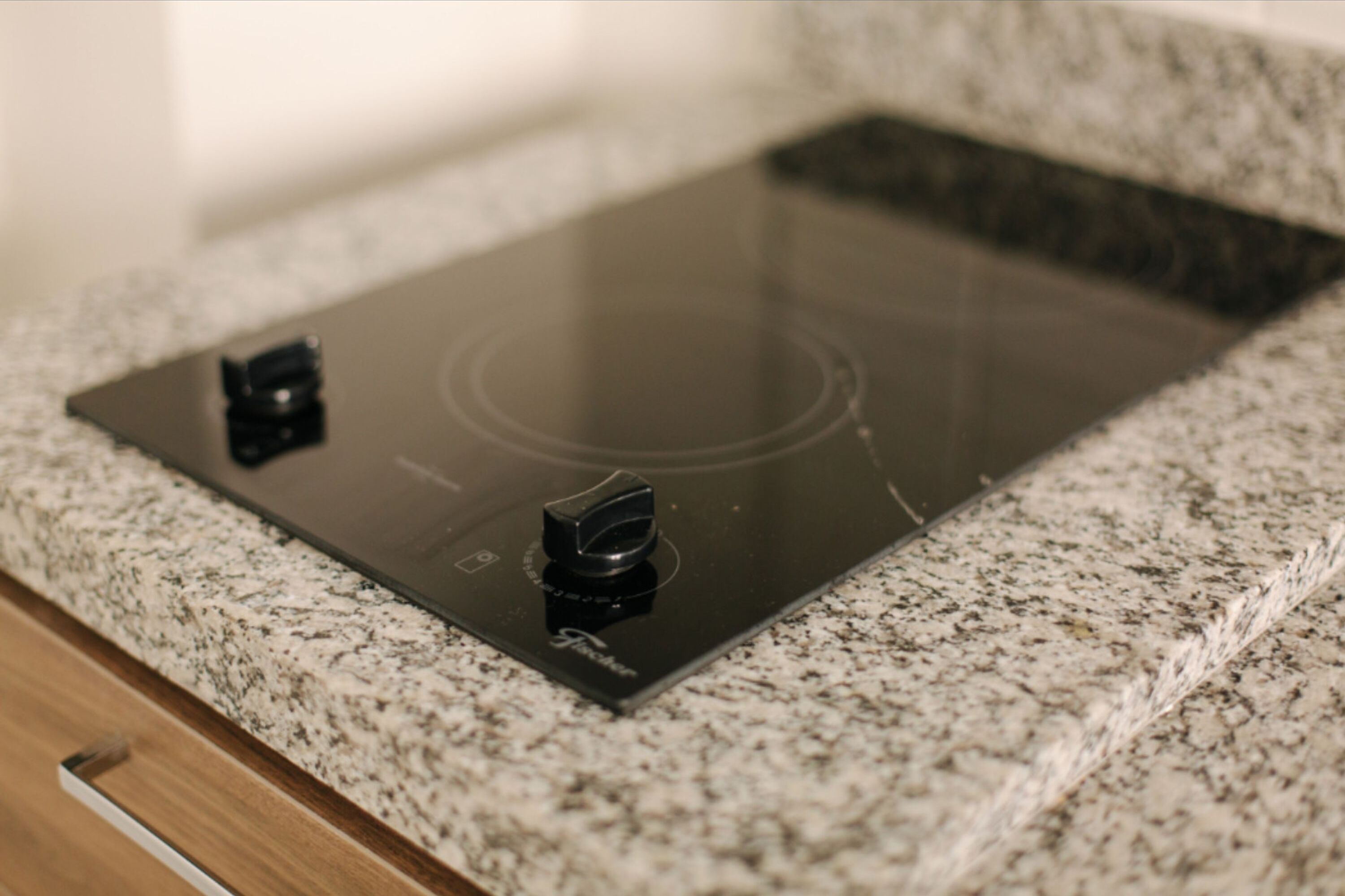 A kitchen with a black induction cooktop on a granite countertop.