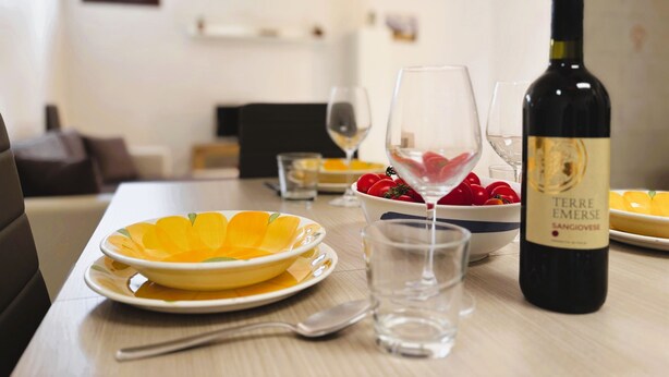 A dining table with plates of food, glasses, and a bottle of wine. - Casa Amodei 2 a Pochi Passi dal Mare (San Vito Lo Capo)