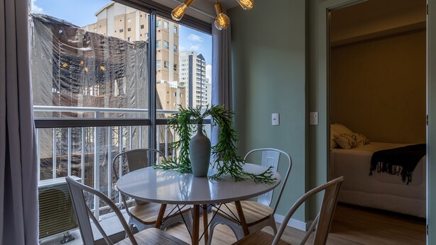 A modern apartment with a balcony, a dining table with chairs, a potted plant, and a bed with a blanket. - Sa1342-514 in S o Paulo (São Paulo)