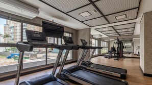 A gym with treadmills, weight machines, and a large window with a view of buildings. - Sa1342-514 in S o Paulo (São Paulo)