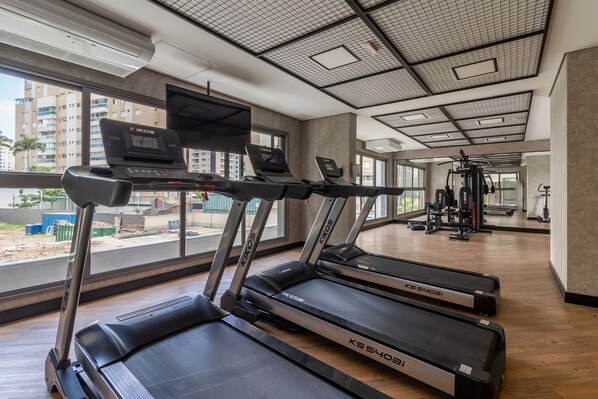 Una palestra con tapis roulant, macchinari per pesi e un'ampia vetrata vista edifici.
